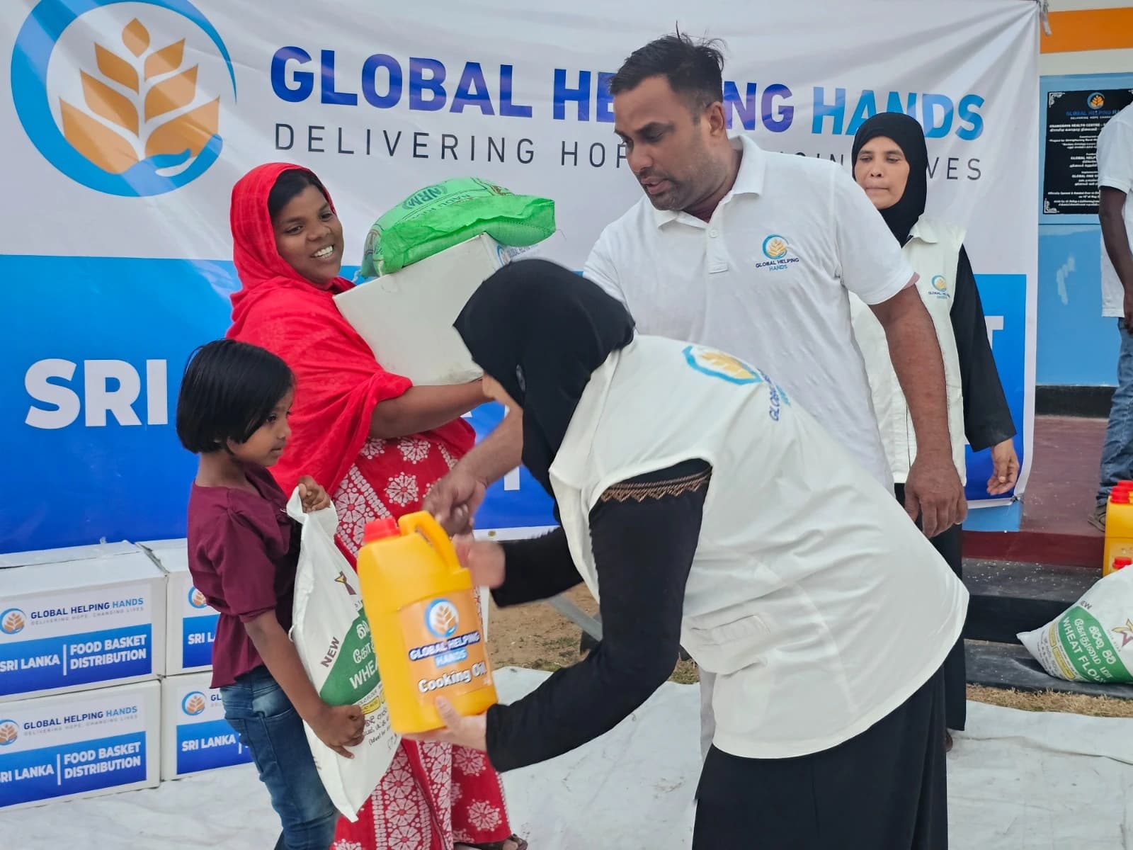 Volunteers handing food baskets and cooking oil to a mother and child at the Global Helping Hands Sri Lanka food basket distribution